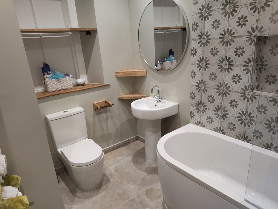 Toilet, pedestal basin and P-shaped bath below patterned wall tiles